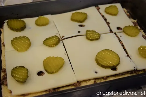 Pickle slices on top of Swiss cheese in a pan.