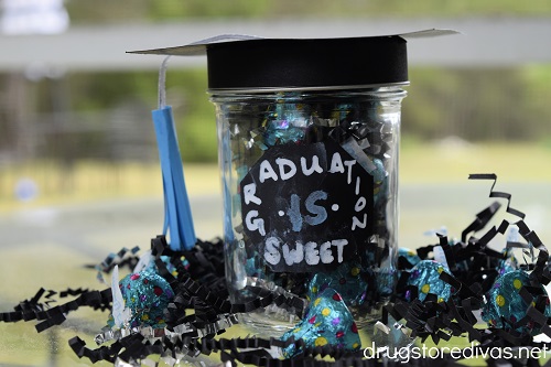 A graduation cap mason jar craft surrounded by candy and paper shred.