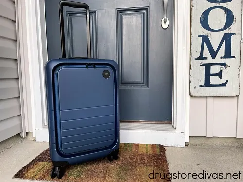 A suitcase on a doormat in front of a door.