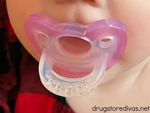 A pink pacifier in a baby's mouth.