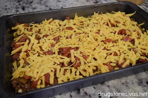 Shredded cheese on top of diced tomatoes in a cake pan.