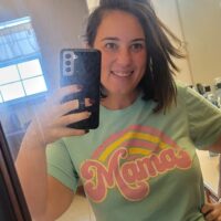 A woman taking a mirror selfie in a shirt that says mama and the words 