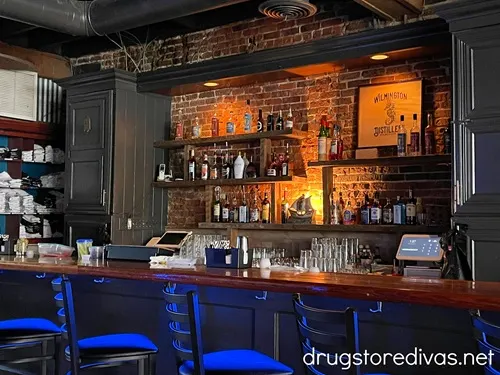 The bar with chairs, lit blue by a light, and bottles behind the bar at Wilmington Distillery in Wilmington, NC.