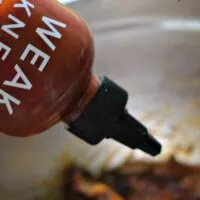 How sauce being poured on chicken wings with the words 