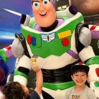 Two boys posing with a Buzz Lightyear character in front of a Lightyear movie poster and the words 