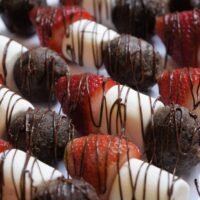 Chocolate Munchkins, marshmallows, and strawberries, drizzled with chocolate, on skewers on a tray with the words 