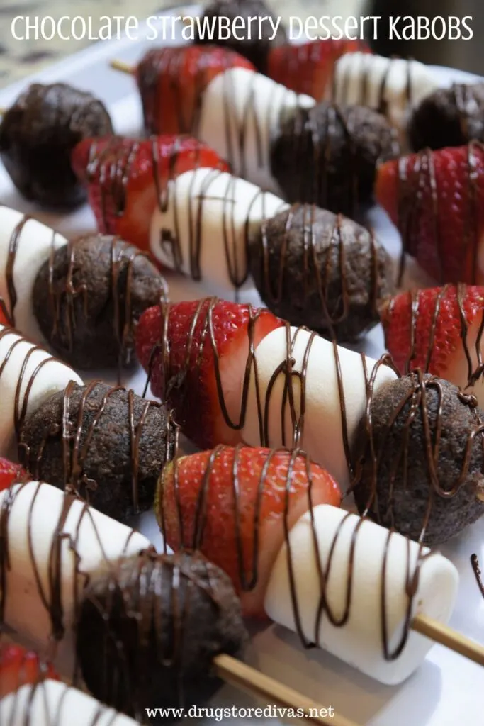 Chocolate Munchkins, marshmallows, and strawberries, drizzled with chocolate, on skewers on a tray with the words "Chocolate Strawberry Dessert Kabobs" digitally written on top.