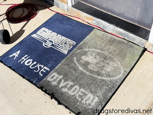 A doormat with the New York Giants logo on the left and New York Jets on the right with the words "A House Divided" under it in front of a door.