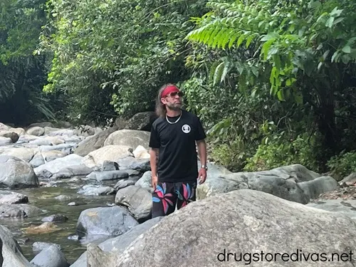 A man, wearing a red cooling towel on his head, standing amongst rocks and trees in the El Yunque Rainforest in Puerto Rico.