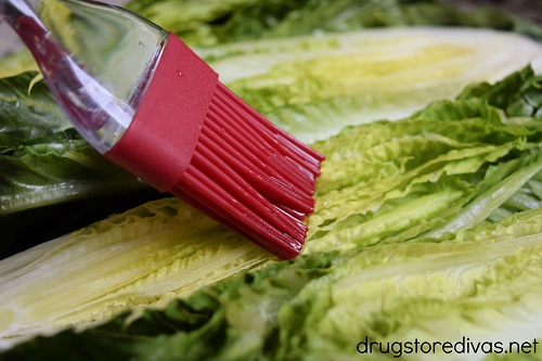 Olive oil being brushed on romaine lettuce with a pastry brush.