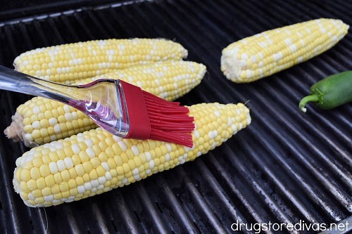 Corn on the grill being brushed by a pastry brush.