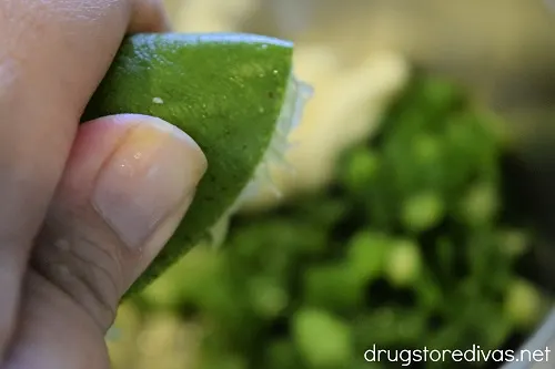 A lime being squeezed over ingredients in a bowl.