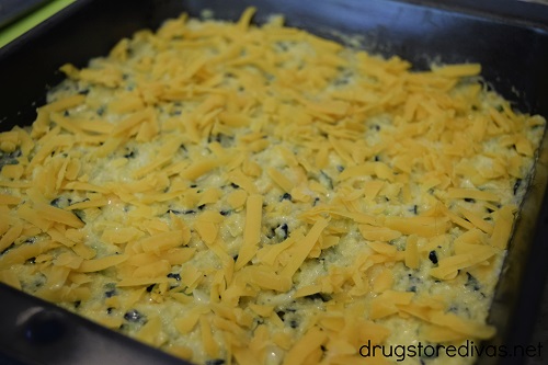Cheddar cheese on top of uncooked Cheesy Zucchini Cornbread Casserole in a pan.