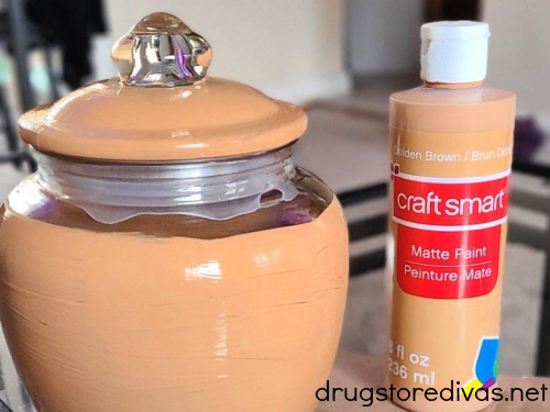 A jar partially painted light brown next to a bottle of light brown paint.