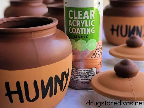 A spray can of clear acrylic paint on a table with DIY Winnie The Pooh Honey Jars.