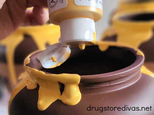 Yellow acrylic paint being poured onto a brown jar.