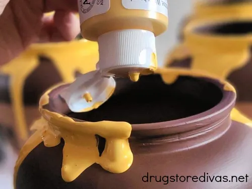 Yellow acrylic paint being poured onto a brown jar.