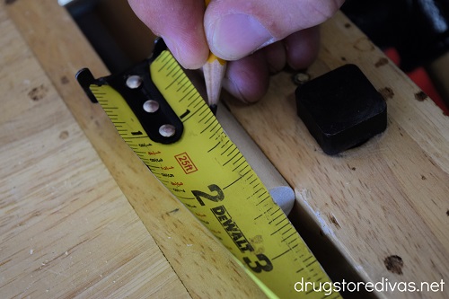 A tape measure measuring a wooden dowel that's being marked with a pencil.