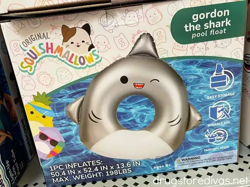 A Squishmallows shark pool float in a box on a shelf in a store.