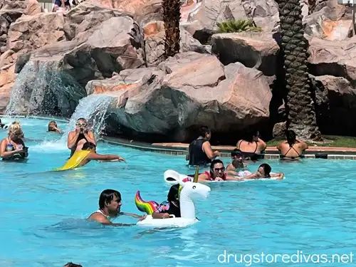 A pool filled with swimmers with the focus of the photo on a girl riding a unicorn pool float.