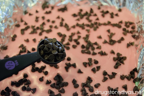 Mini chocolate chips being poured into pink fudge.