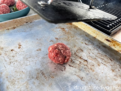A ball of meat about to be smashed by a bacon press.