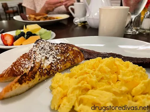 Eggs and toast on a plate with fruit behind it.