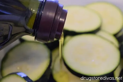 Olive oil being poured on zucchini slices.