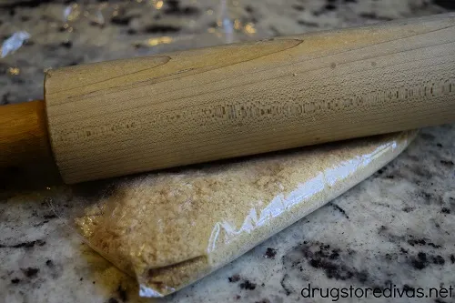 A rolling pin on top of a bag of graham cracker crumbs.