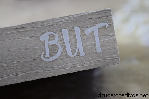 The word "BUT" on a piece of wood.