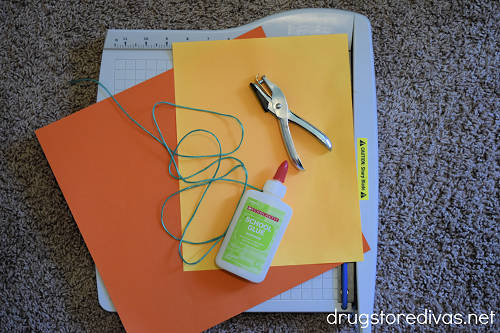 A paper trimmer, orange scrapbook paper, green twine, glue, and a single hole punch.