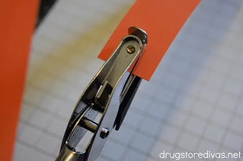 An orange strip of paper being hole punched by a single hole punch.