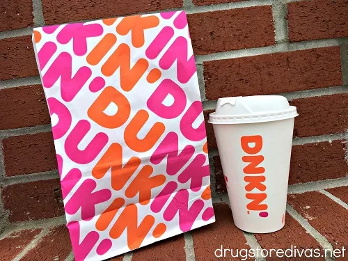 A Dunkin' bag and coffee cup against a brick wall.