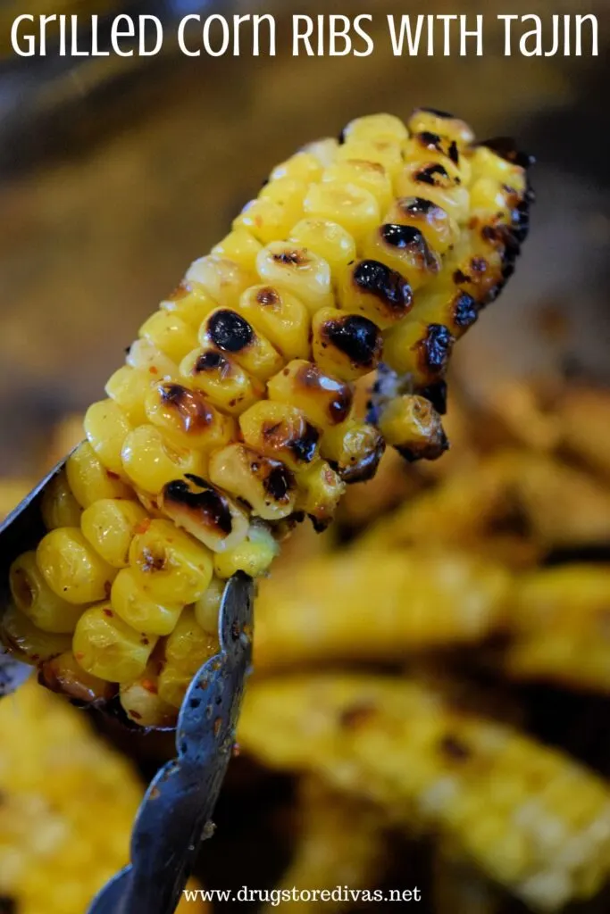 A pair of tongs holding a corn rib above a bowl of them with the words "Grilled Corn Ribs With Tajin" digitally written on top.