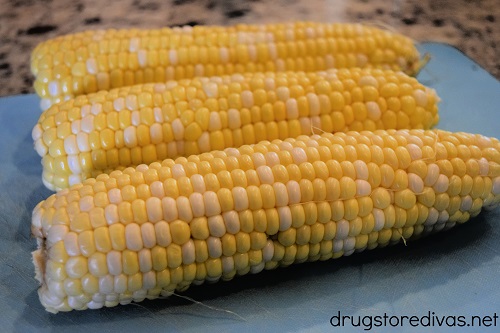 Three ears of corn on a cutting board.