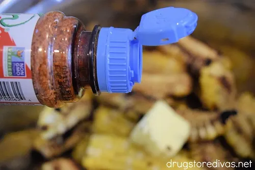 Tajin being sprinkled on corn ribs in a bowl with a pat of butter on top.