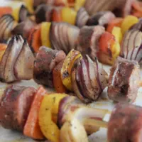 Five sausage and veggie skewers on a plate with the words 