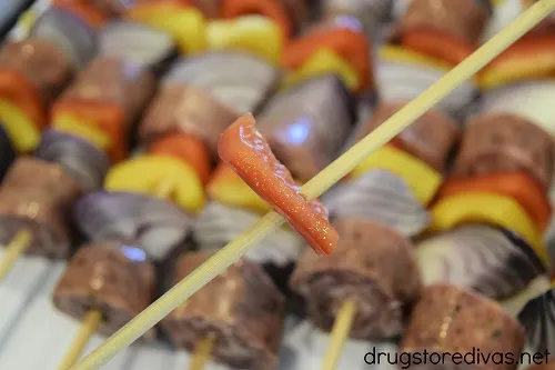 A piece of red pepper on a skewer, hovering over completed sausage kabobs.
