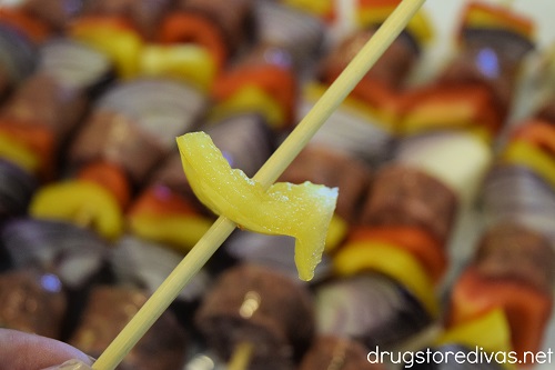 A piece of yellow pepper on a skewer, hovering over completed sausage kabobs.