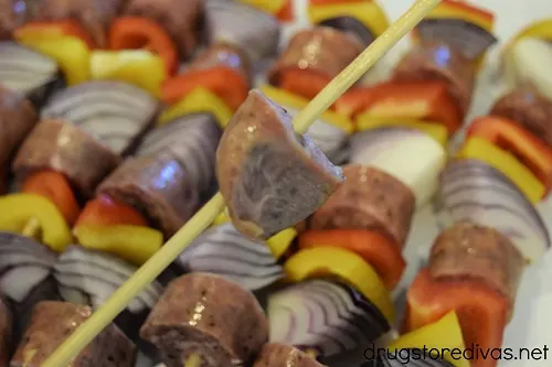 A piece of sausage on a skewer, hovering over completed sausage kabobs.