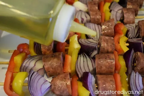 Sausage and vegetable skewers being drizzled with olive oil.