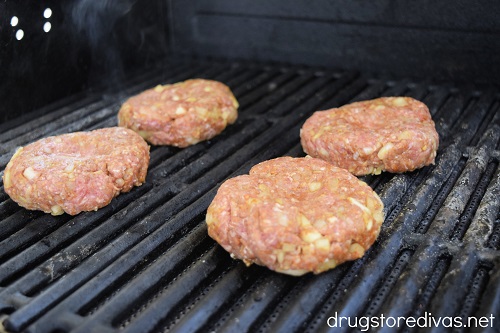 Four raw burger patties on a grill.