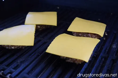 Four burger patties with cheese on a grill.