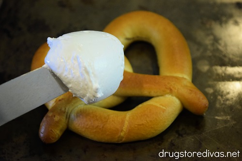 Marshmallow creme on a knife above a soft pretzel.