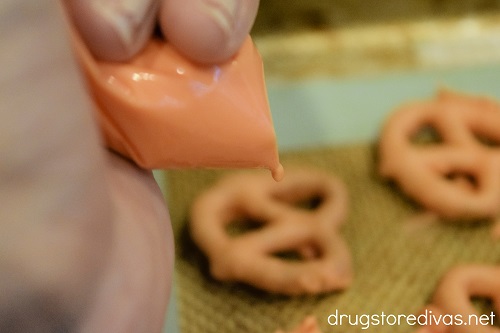 Melted orange candy melts in a piping bag being drizzled on orange pretzel twists.