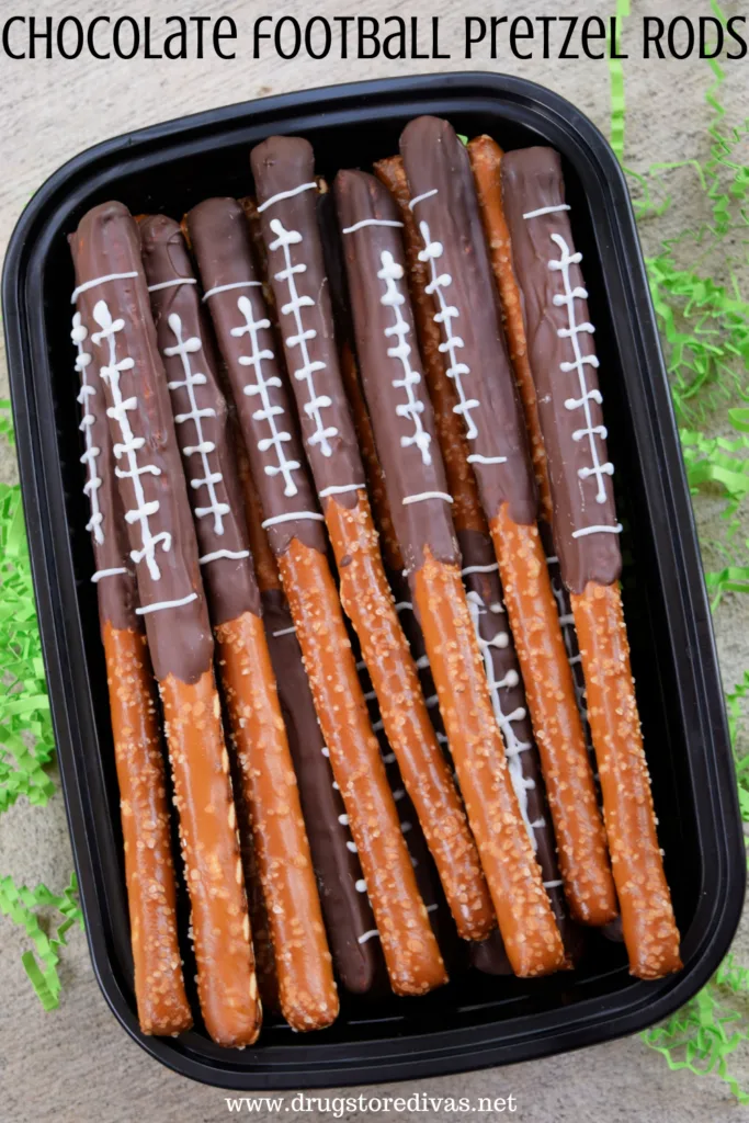 Chocolate-covered pretzels, decorated to look like footballs, in a container with the words "Chocolate Football Pretzel Rods" digitally written on top.