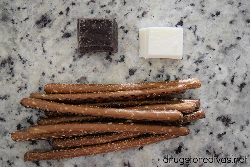 A piece of chocolate almond bark, a piece of vanilla almond bark, and pretzel rods.