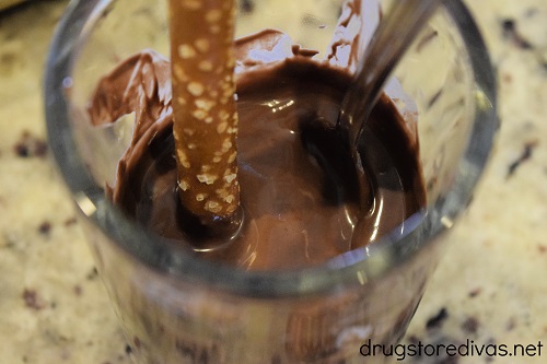 A pretzel rod being dipped into melted chocolate.