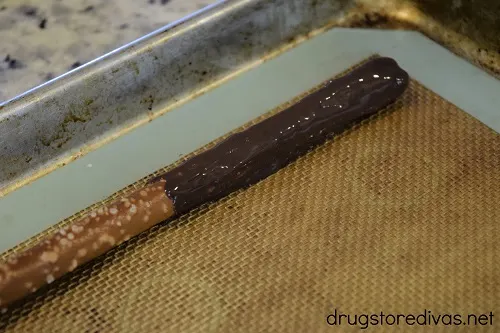A chocolate dipped pretzel on a silicone baking mat-lined cookie sheet.