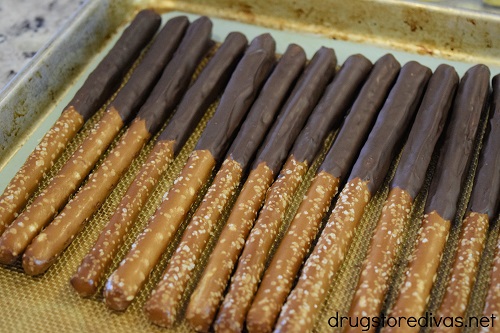 Many chocolate dipped pretzels on a silicone baking mat-lined cookie sheet.